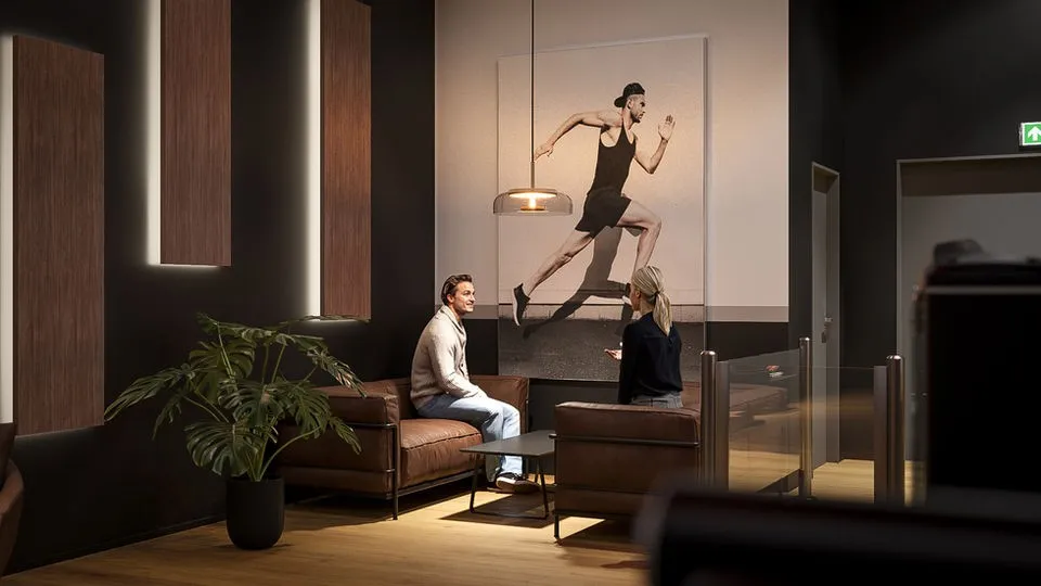 3D-Visualisierung einer Studio-Lounge mit Ledersofas, Pendelleuchte und großem Wandbild eines Läufers